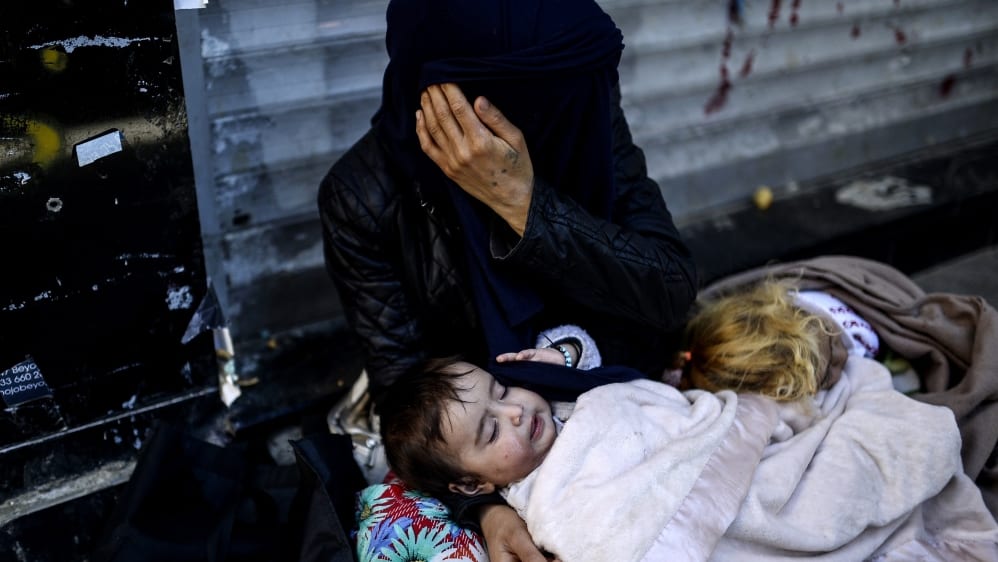 A Syrian Kurdish refugee woman with her daughter waits for help, abandoned and alone