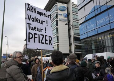 A demonstrator holds a sign reading Scammer, thief, killer, Pfizer & at Macron during a protest in front of the Pfizer headquarters in Paris