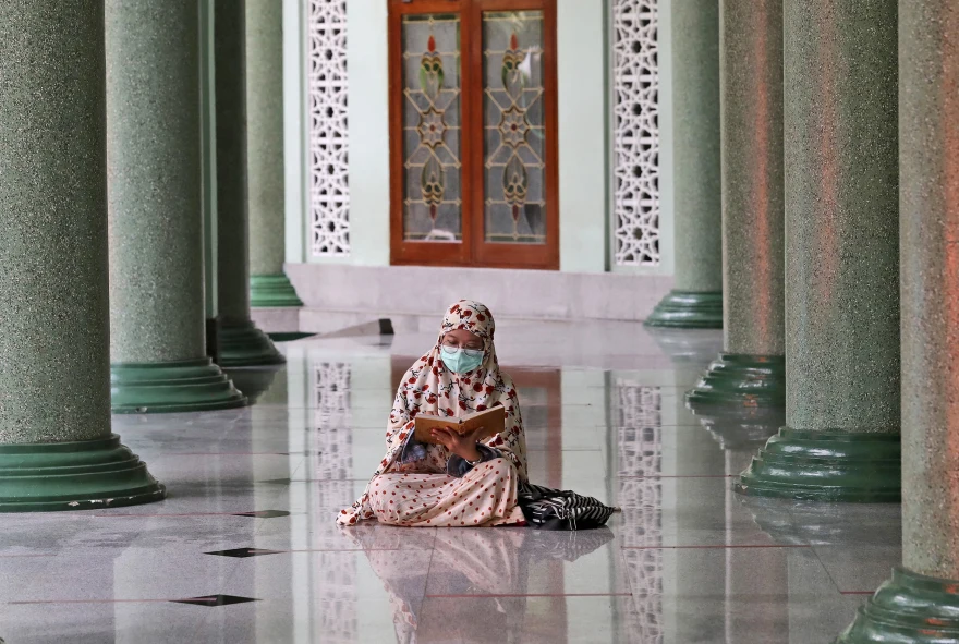 A worshipper reads the Quran while waiting to break her fast during the first day of Ramadan, at a mosque in Jakarta, Indonesia