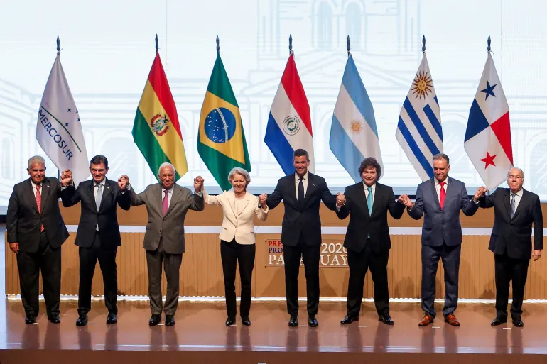 Leaders from South American nations and European Commission President Ursula von der Leyen stand in front of flags and hold hands