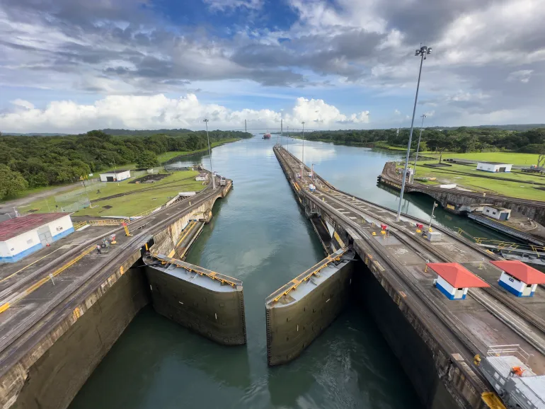 Aerial perspective of the Panama Canal's Miraflores Locks system, showing the massive water chambers and lock gates. The engineering marvel demonstrates the canal's essential role in global maritime commerce, with its distinctive green-tinted water contrasting against the concrete structure.