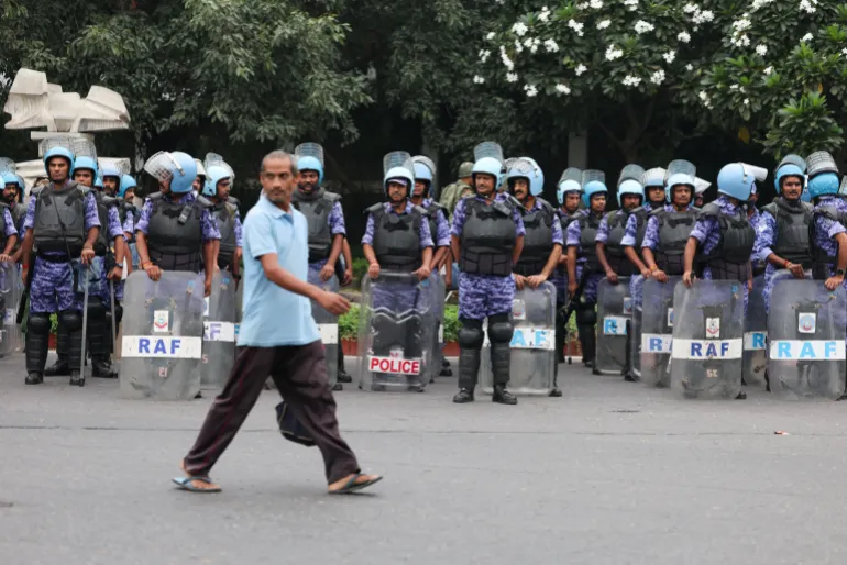 A man walks past members of the Rapid Action Force (RAF) standing guard ahead of a protest planned by the Cockroach Janta Party (CJP) seeking the resignation of India’s Chief Election Commissioner Gyanesh Kumar, in New Delhi, India, October 10, 2026
